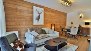 A modern living room with a wooden wall, a sofa, a coffee table, and a dining area with chairs and a table. - Wifi, Ground floor, balcony, tv, 43m², Les Gets (Les Gets)