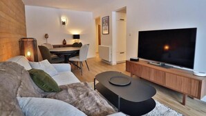 A modern living room with a flat-screen TV, a sofa, a coffee table, and a dining area with a table and chairs. - Wifi, Ground floor, balcony, tv, 43m², Les Gets (Les Gets)
