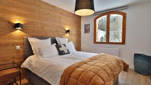 A bedroom with a wooden headboard, a bed with white bedding and a brown quilt, two wall-mounted lights, a window with a view of trees, and a radiator. - Wifi, Ground floor, balcony, tv, 43m², Les Gets (Les Gets)