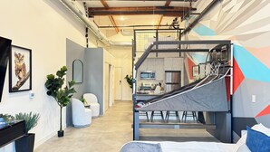Ein modernes Schlafzimmer mit einem Etagenbett, einem Schreibtisch und einem Stuhl. Eine Treppe mit einem Netzgeländer führt zu einem Schlafbereich auf Podest.
