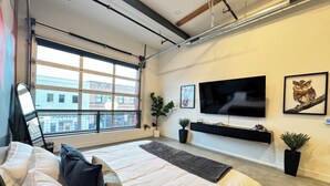 Ein modernes Schlafzimmer mit einem großen Bett, einem an der Wand montierten Fernseher und einem Fenster mit Blick auf die Stadt.
