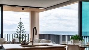 A modern kitchen with a large island, a dining area with a view of the ocean, and a balcony with a railing. - Ocean Views Palm Beach (Palm Beach)
