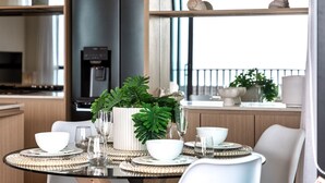 A modern dining area with a round table set for four, featuring white bowls, glasses, and a centerpiece with green foliage. - Ocean Views Palm Beach (Palm Beach)