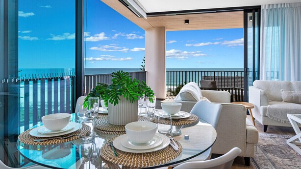 A modern dining area with a glass table, white plates, and bowls, set against a scenic ocean view. - Ocean Views Palm Beach (Palm Beach)