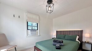 Et soveværelse med seng, to sengeborde, en stol, et vindue med persienner og en loftlampe.