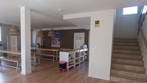 A spacious room with wooden flooring, a staircase, and a dining area with benches and tables.