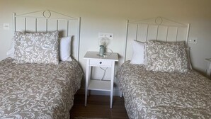 A room with two beds, each with a patterned bedspread and matching pillows. There is a small bedside table with a lamp between the beds.