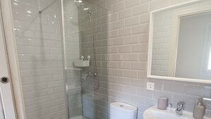 A bathroom with a glass-enclosed shower, a white toilet, a sink with a mirror, and a towel rack.