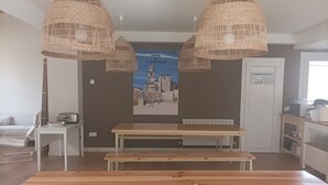 A dining area with a wooden table and bench, wicker pendant lights, a poster on the wall, and a door with a sign.