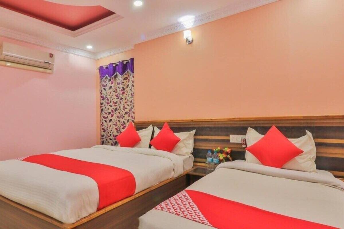 A hotel room with two beds, each with red and white bedding, a ceiling fan, an air conditioning unit, and a decorative curtain.