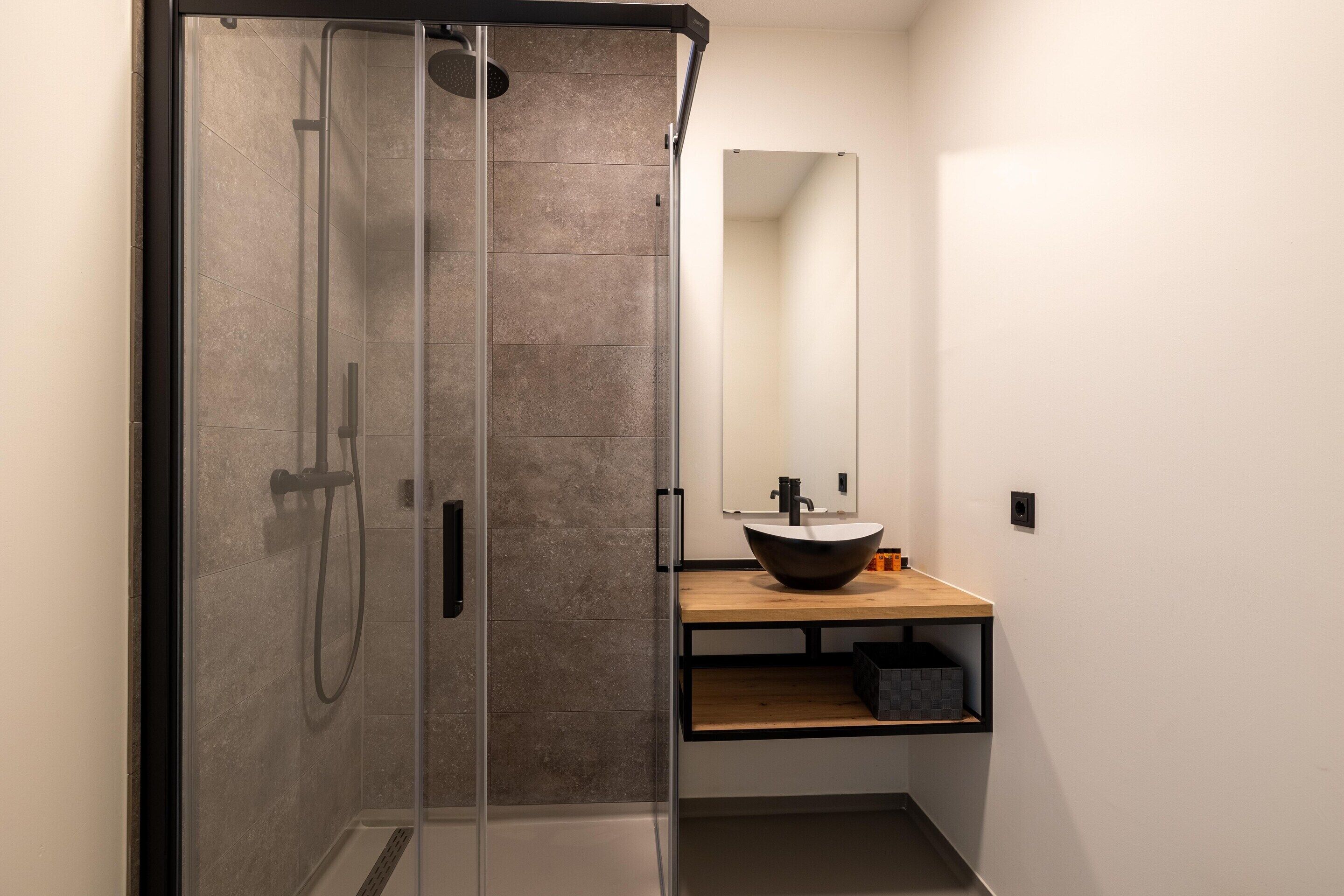 Ein modernes Badezimmer mit einer gläsernen Dusche, einem Holzkosmetikschrank mit Waschlappenbecken und einem großen Spiegel.