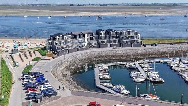 Un port de plaisance situé sur la côte, doté de bâtiments modernes, d’un espace de stationnement et d’un ensemble de bateaux.
