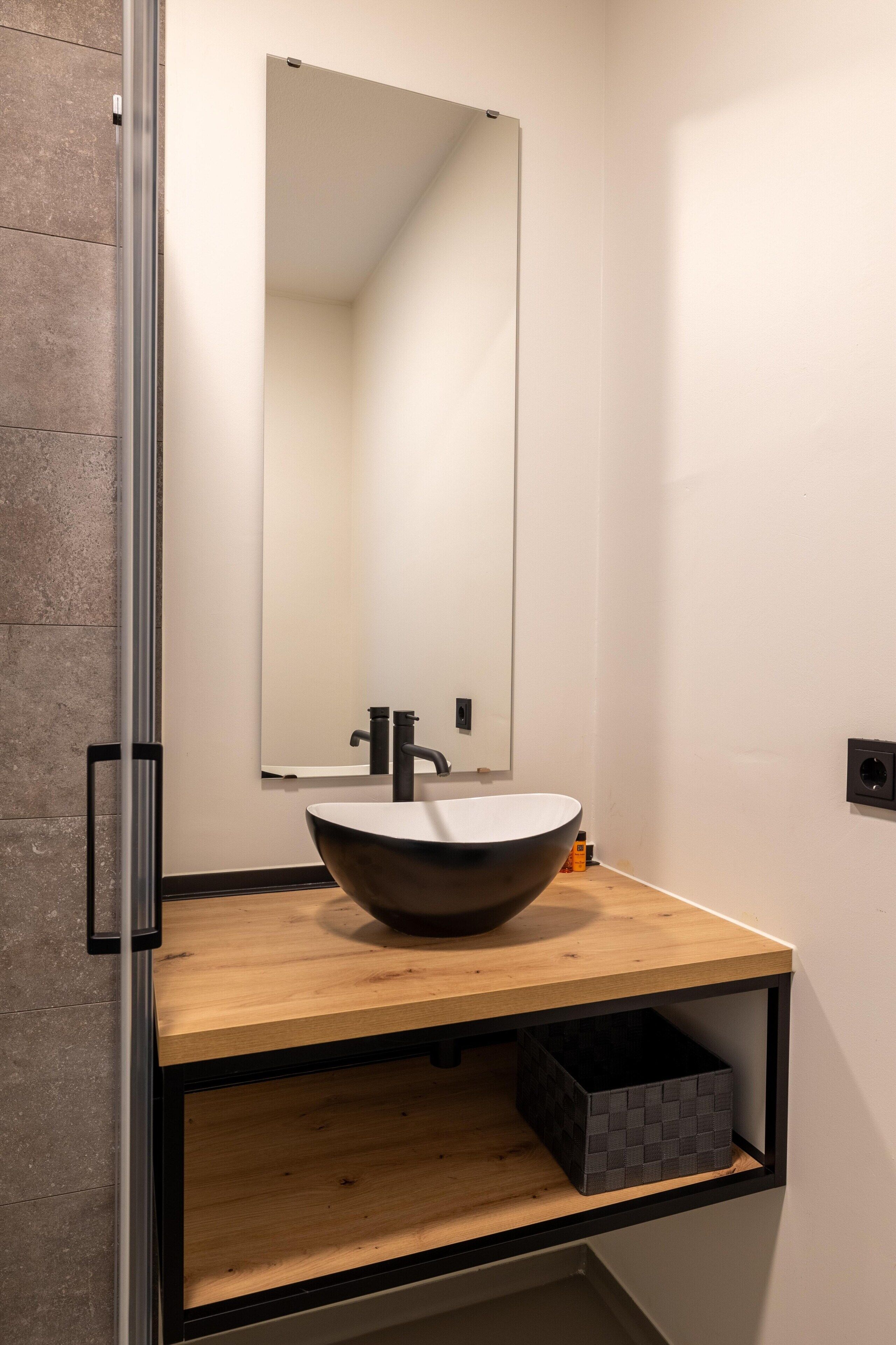 A modern bathroom with a large mirror, a wooden vanity, and a black storage box.