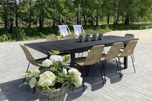 An outdoor dining area with a black table and wicker chairs, surrounded by greenery. - Comfortable Holiday Homes With a Summer Pool (Mielno)