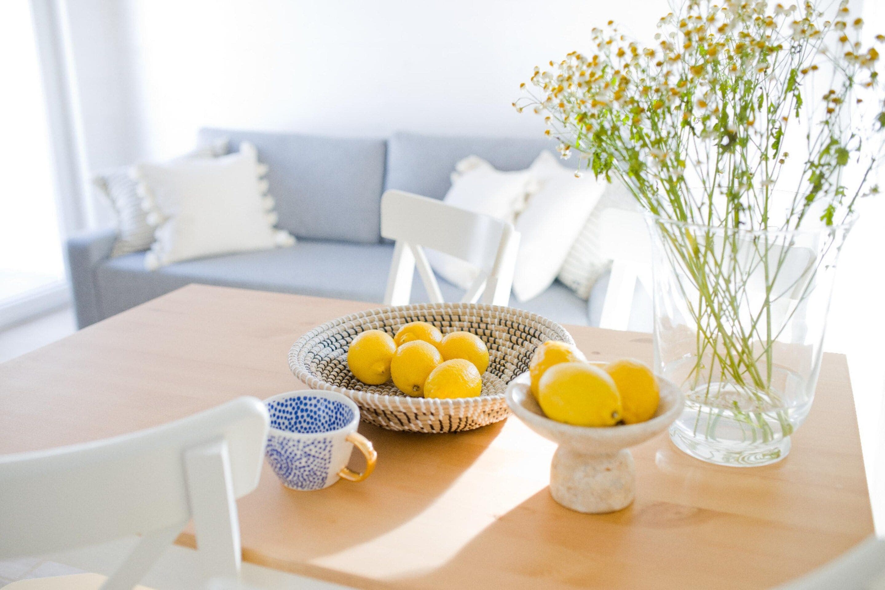 Une table à manger ornée d’un panier tressé rempli de citrons, d’un petit bol de citrons et d’un vase transparent contenant des fleurs.
