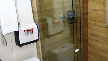 Casa de banho com cabine de duche em vidro, sanita branca e toalheiro com um aviso.