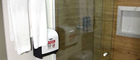 A bathroom with a toilet, a glass shower enclosure, and a towel rack with folded towels.