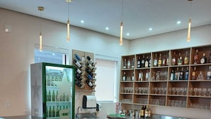 A bar area with wooden bar stools, a refrigerator stocked with bottles, and shelves with glasses and liquor bottles. - HOTEL INTERNACIONAL GUARULHOS (Guarulhos)