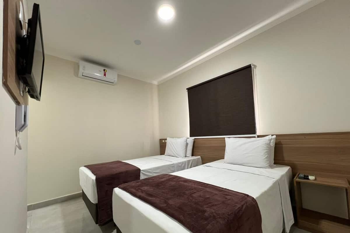 A hotel room with two single beds, a TV mounted on the wall, an air conditioning unit, and a wooden headboard.