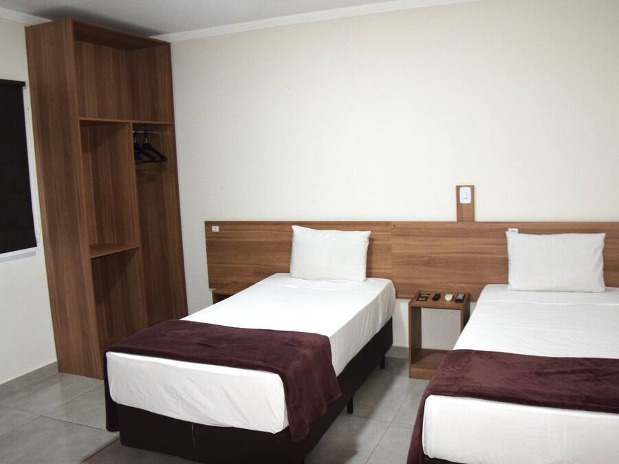A hotel room with two beds, a wooden wardrobe, and a small bedside table with a phone and a remote control.