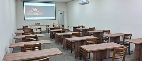 Un aula con escritorios y sillas de madera, una pantalla de proyector y un proyector instalado en el techo.