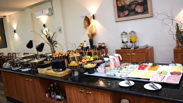 A buffet setup with various food items and beverages, a mirror, and a painting on the wall. - HOTEL INTERNACIONAL GUARULHOS (Guarulhos)