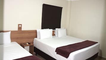 A hotel room with two beds, a wooden headboard, a dark-colored window blind, and a small bedside table with a remote control.