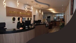 A hotel reception desk with a modern design, a clock, and a sign indicating the hotel name. - HOTEL INTERNACIONAL GUARULHOS (Guarulhos)