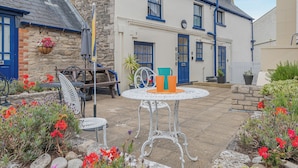 A courtyard with a round table, chairs, and a bench. There are potted plants and flowers around the seating area. - 1 bedroom accommodation in Swanage (Swanage)