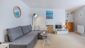 A modern living room with a grey sofa, a small round table, a TV, and a wooden cabinet. - 1 bedroom accommodation in Swanage (Swanage)