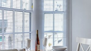 A dining table set with white plates, a wine bottle, and glasses, positioned near a window with blinds. - 1 bedroom accommodation in Swanage (Swanage)