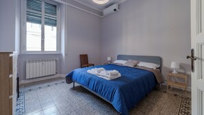 A bedroom with a bed, a radiator, a window with blinds, a chair, a bedside table with a lamp, and a door. - Sabina House a 10-minute walk from the Sistine Chapel and St. Peter's. (Roma)