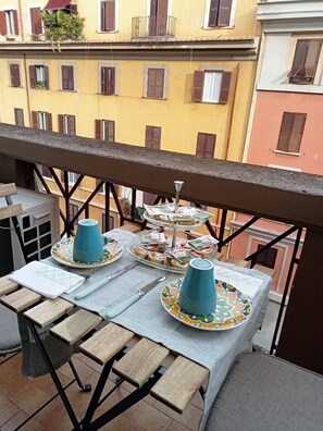 A balcony with a table set for two, featuring a blue mug, a plate with snacks, and a small tray of snacks.