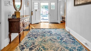 Un couloir avec un tapis à motifs, des meubles en bois et une porte donnant sur l’extérieur.