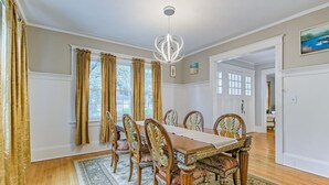 Une salle à manger avec une longue table en bois, des chaises décorées et un lustre.