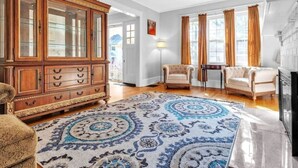 Un salon spacieux comprenant un grand meuble en bois, deux fauteuils, un canapé et un tapis à motifs.
