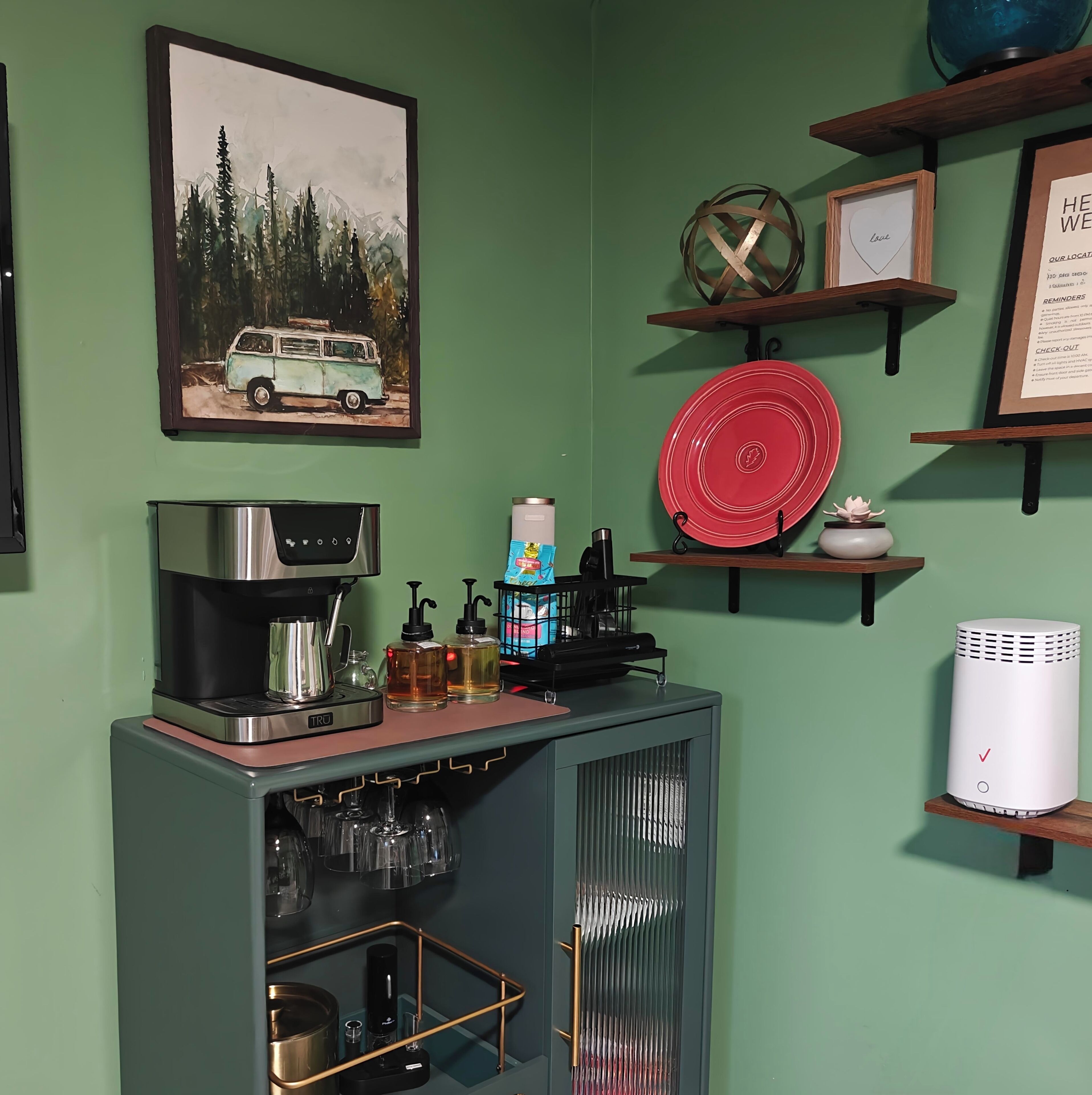 Ein Küchenbereich mit einer Kaffeemaschine, einem roten Teller und einem gerahmten Bild an der Wand.