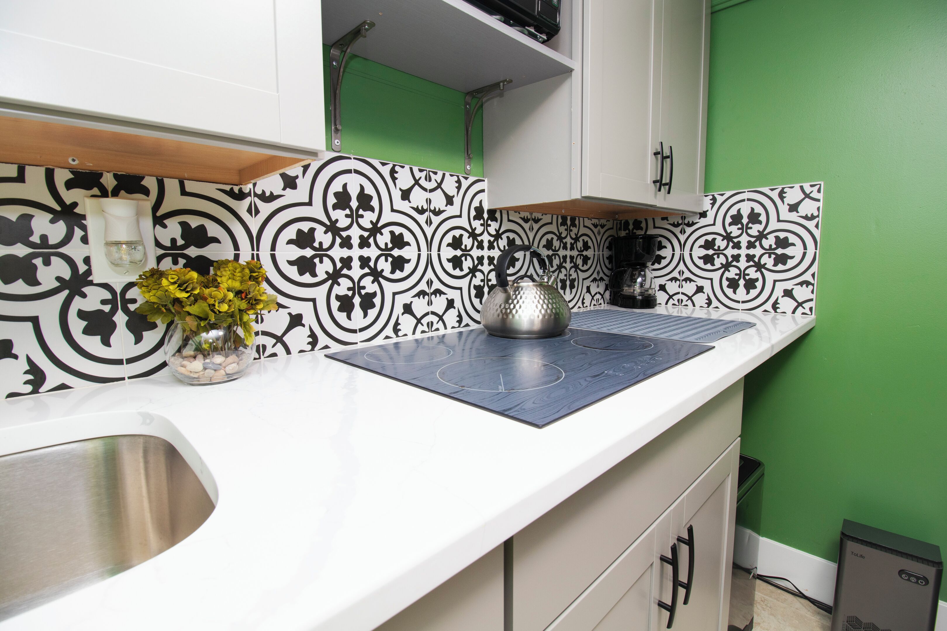 Une cuisine avec un crédence à motifs noir et blanc, un évier en acier inoxydable, une bouilloire et un petit vase avec des fleurs.