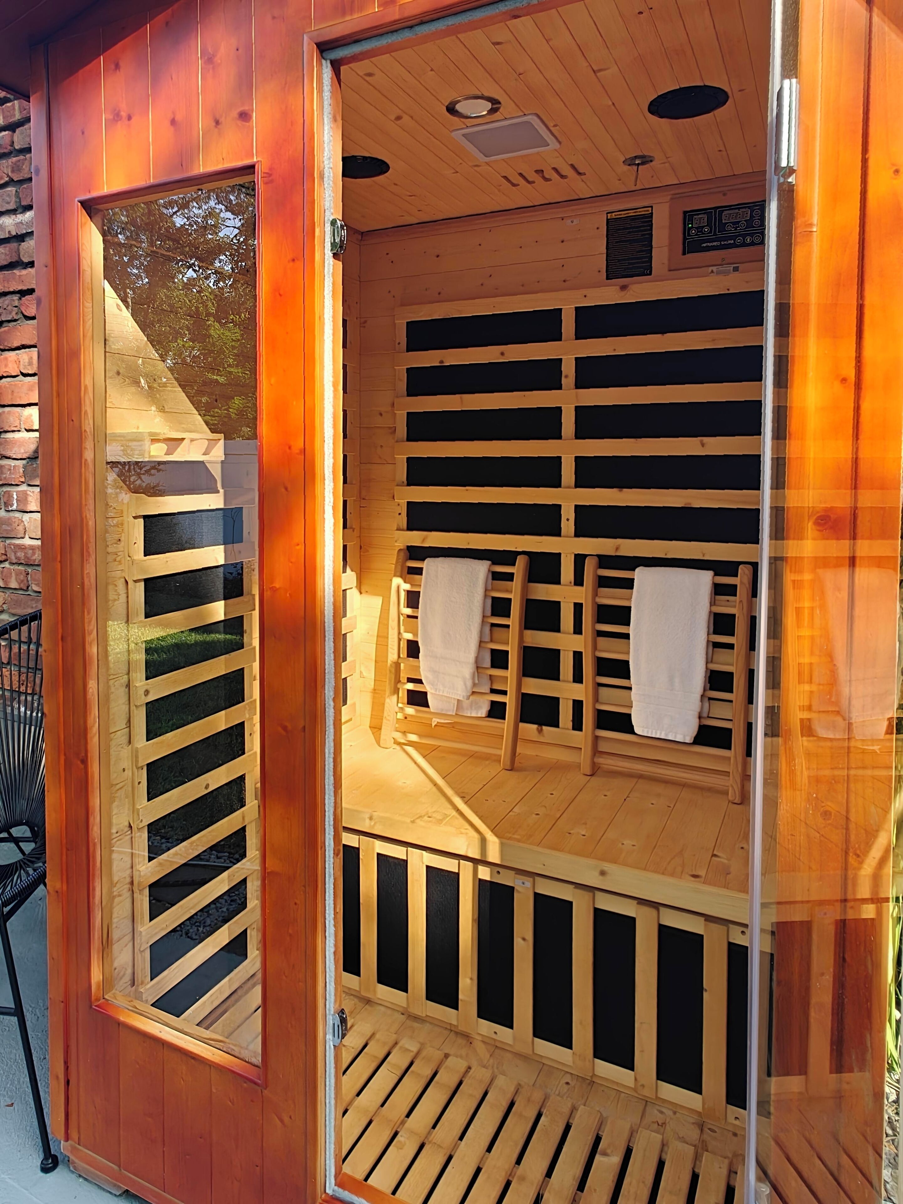 A sauna with wooden benches and a glass door, featuring a control panel on the wall.