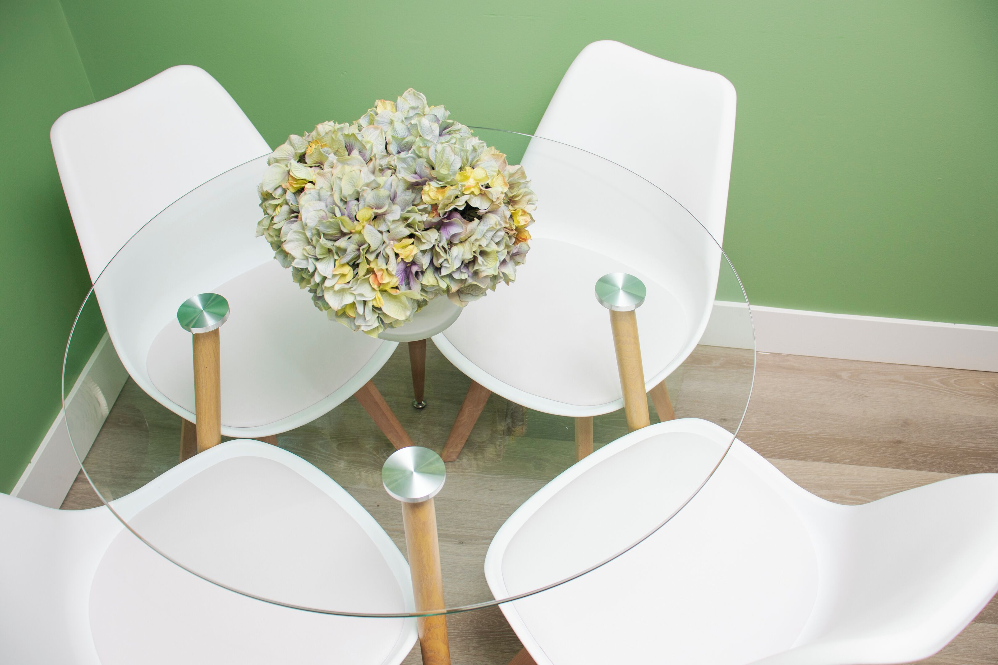 A dining area with a round glass table surrounded by white chairs with wooden legs.