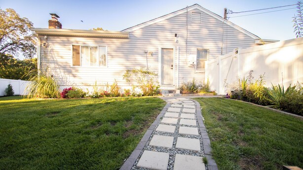 Una casa amb un camí pavimentat que condueix a la porta principal, envoltada d'un jardí ben cuidat i diferents plantes.