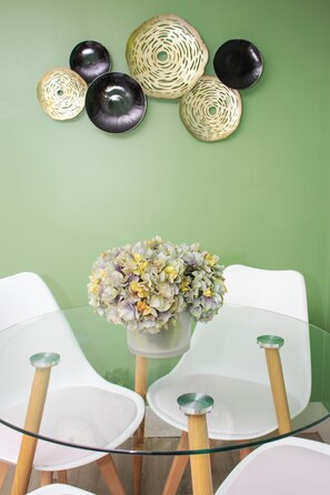 A dining area with a glass table surrounded by white chairs, a vase of flowers, and decorative plates on the wall. - Central 2BR, Garden Suite, Top Amenities & Care! (Central Islip)