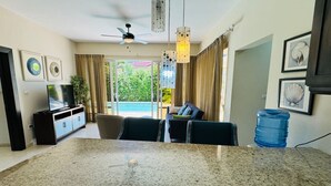 A dining area with a granite table, a ceiling fan, and a view of a balcony with curtains.