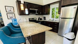 A kitchen with dark wood cabinets, stainless steel appliances, a granite countertop, and a blue upholstered chair.