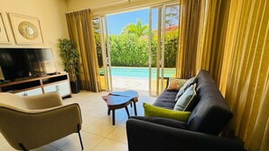 A living room with a sofa, a TV, a coffee table, and a view of a swimming pool through large glass doors.