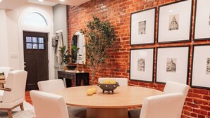 A dining area with a brick wall, framed pictures, and a round wooden table with chairs.