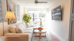 A living room with a sofa, a coffee table with flowers, a lamp, and a TV on the wall.
