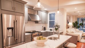 A modern kitchen with stainless steel appliances, a marble countertop, and pendant lighting.