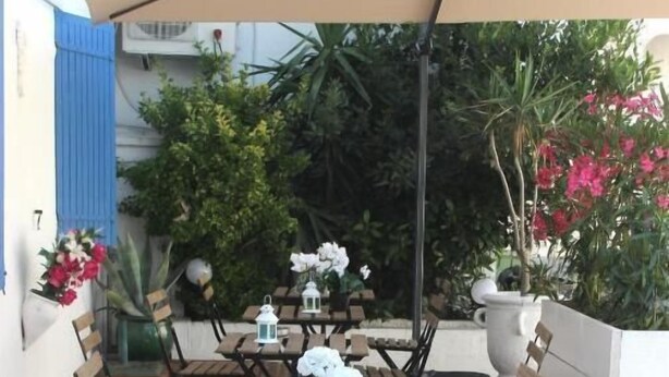 Un patio al aire libre con mesas y sillas de madera, faroles blancos y plantas en macetas.