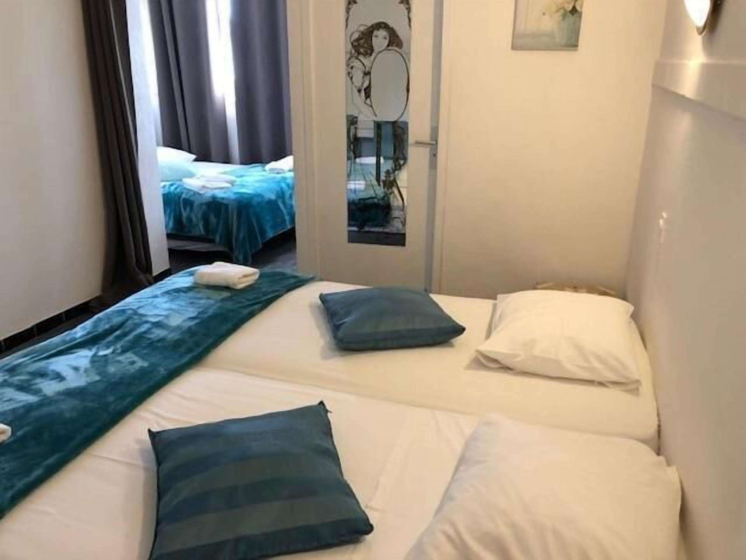 A hotel room with two beds, each with a pillow and a blanket. There is a mirror on the wall and a window with curtains.